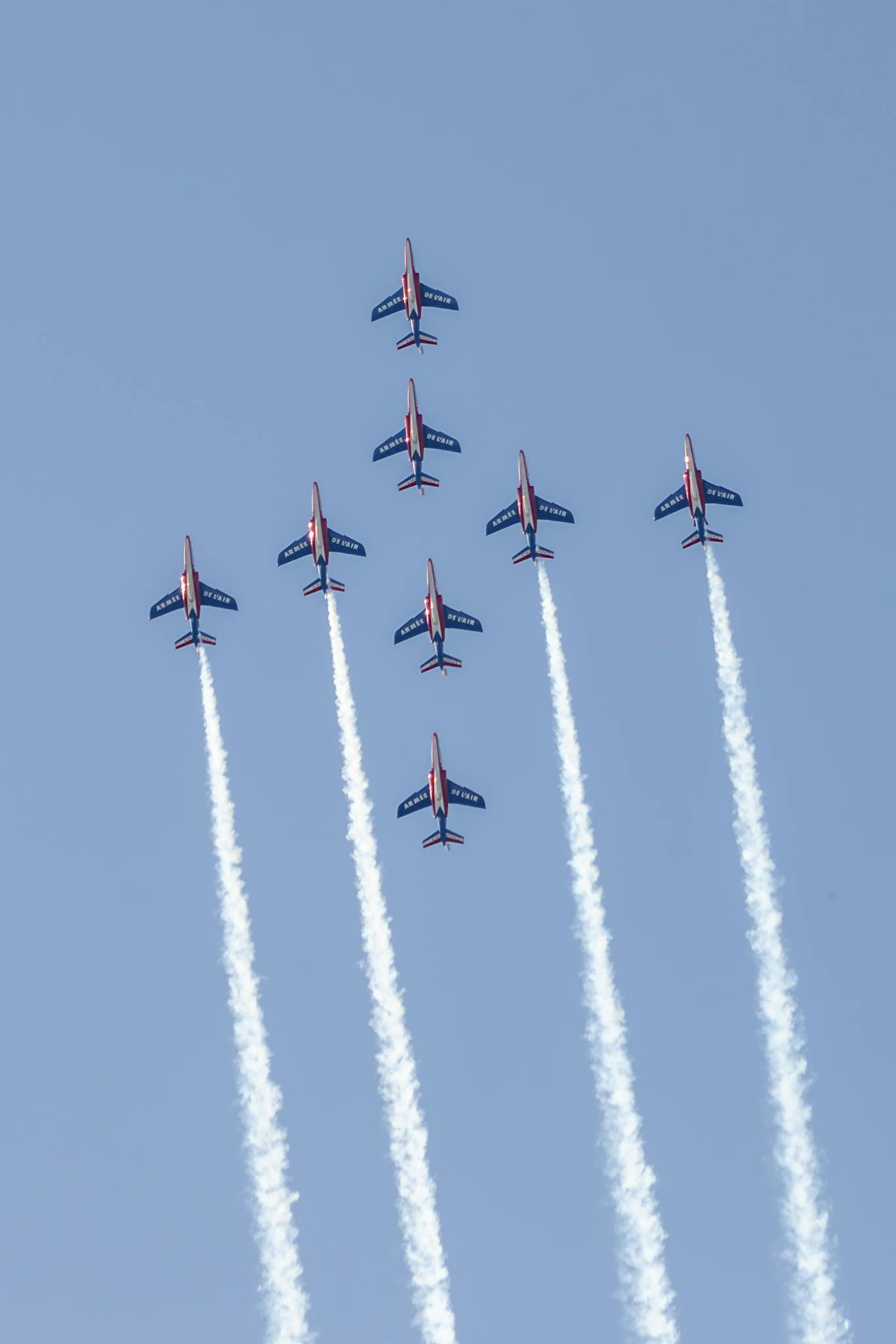Aerial display by Patrouille de France with vibrant smoke trails in a clear blue sky.